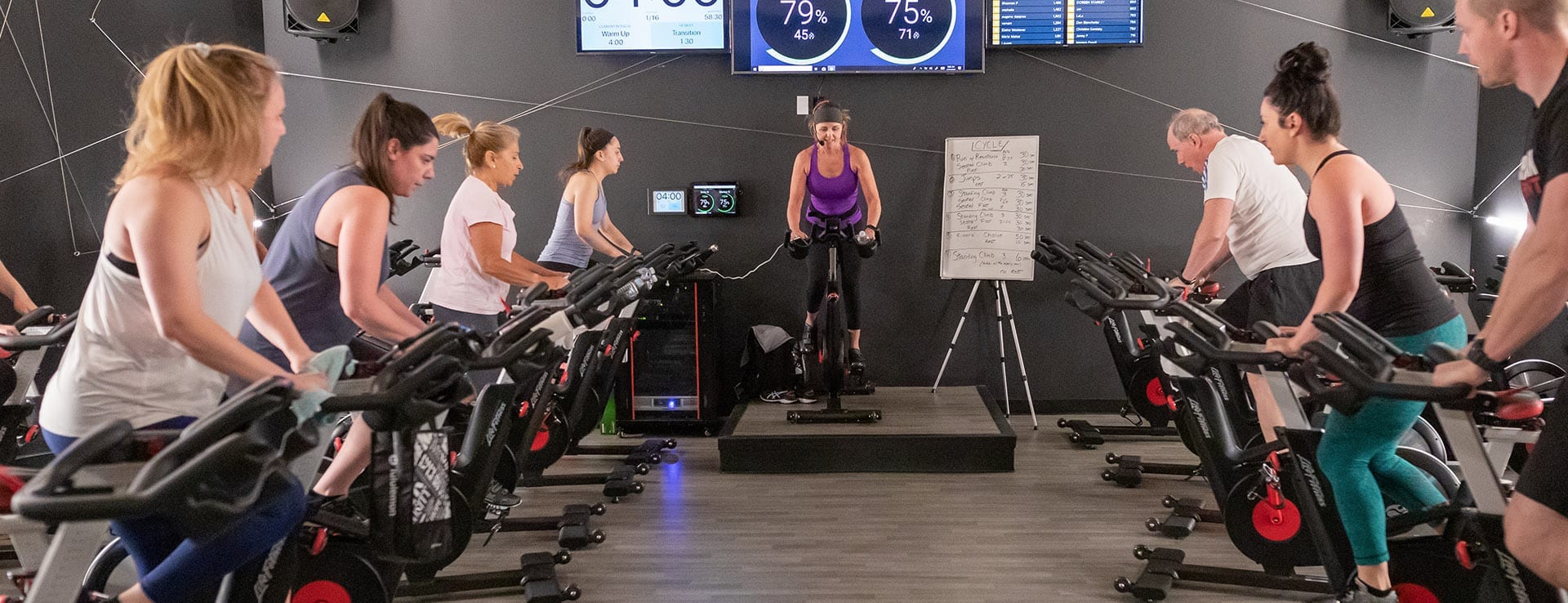 a group of men and women exercising on machines in a spacious gym studio while an instructor motivates them in the best gym near me