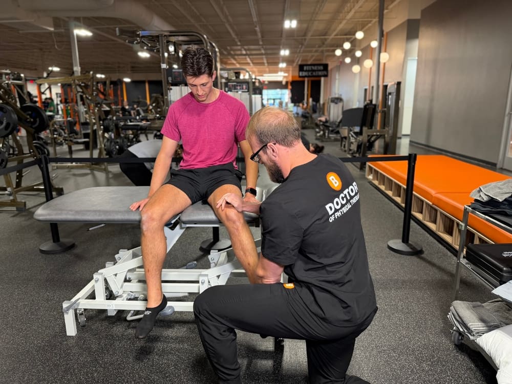 Physical therapist at Best Fitness Woburn helping a member with knee rehabilitation on a treatment table in the gym