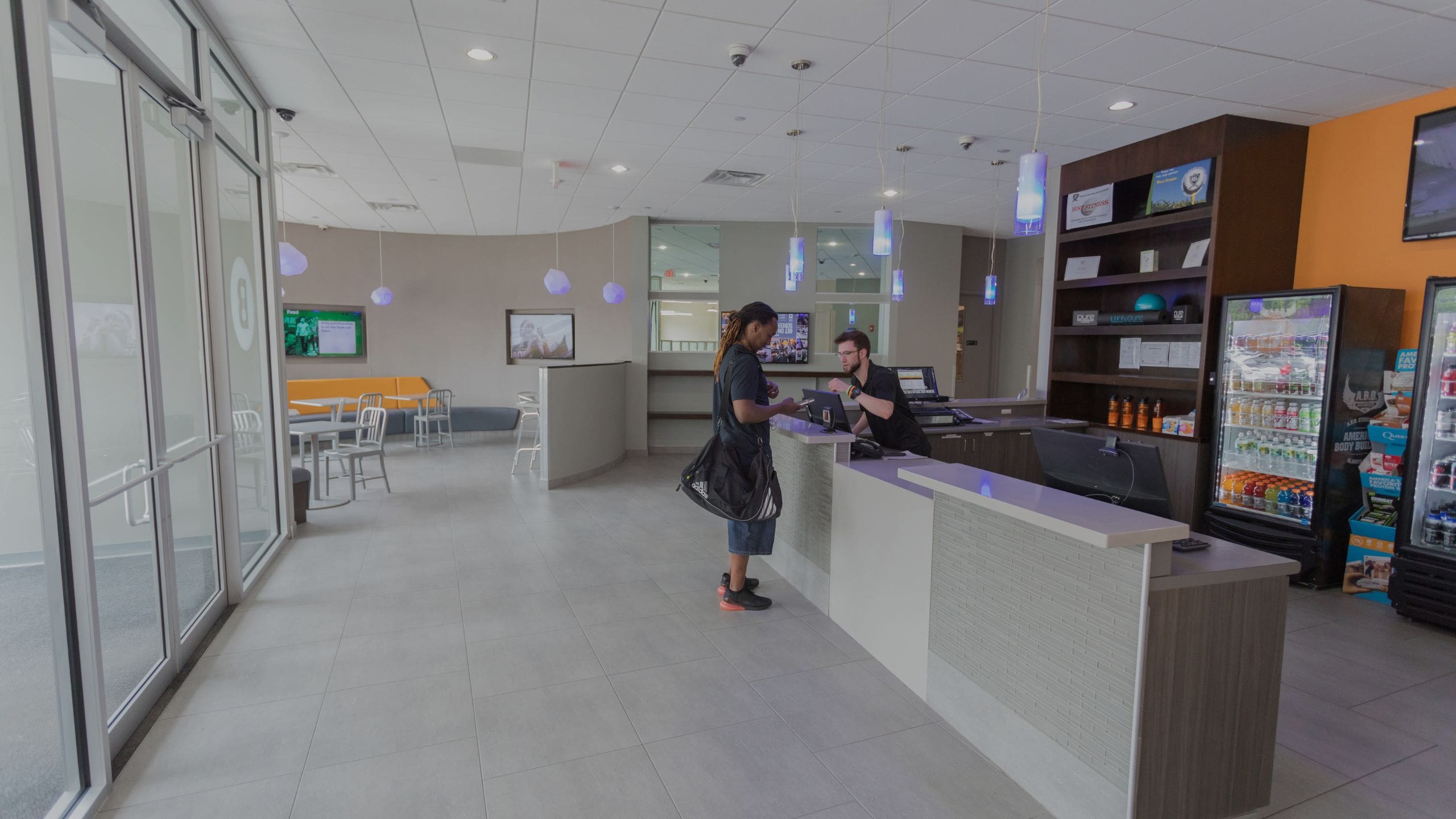 A gym member speaks with an employee at the front desk of a modern gym lobby