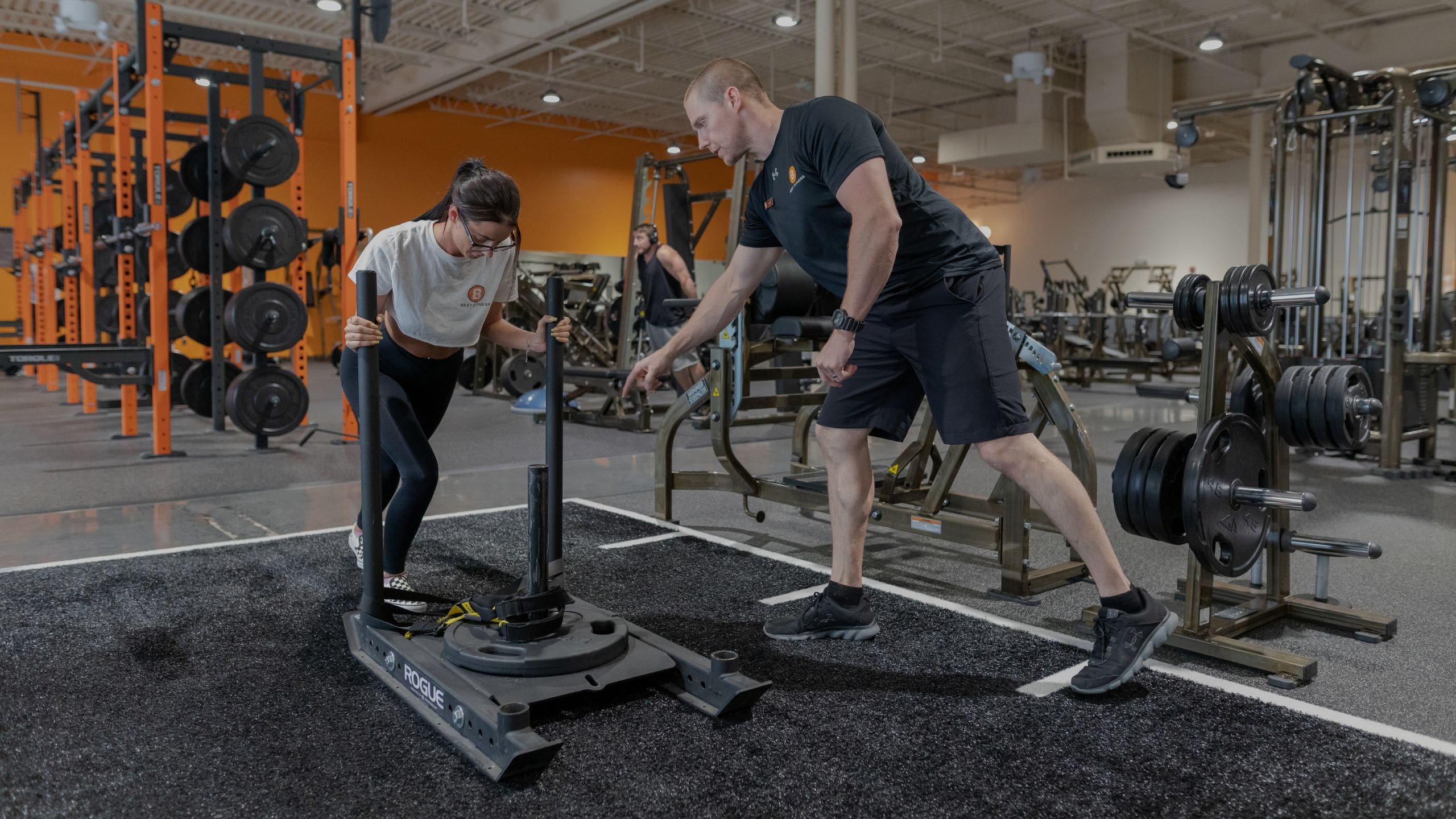 a certified personal trainer spots a gym member during a strength training workout at a best fitness gym near me