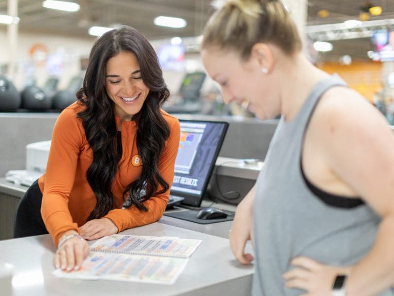 a gym member speaks with a nutritionist at the front desk of a new york gym