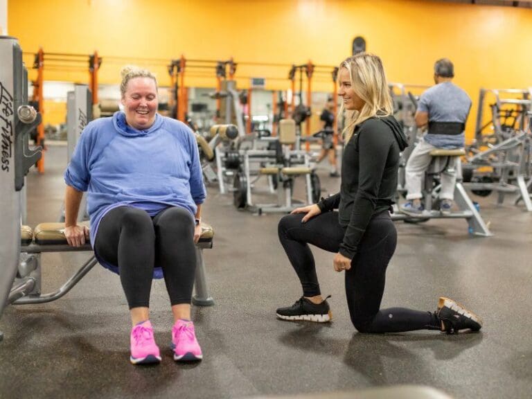 a certified personal trainer spots a gym member during a strength training workout at a best fitness gym near me