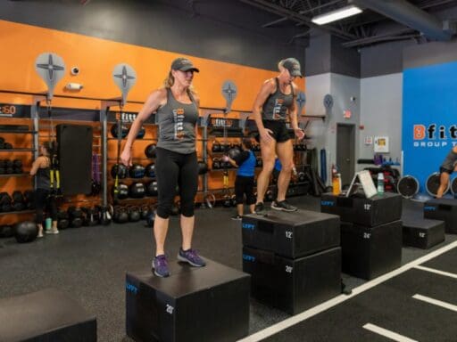 2 gym members do box jumps during a group fitness class in a boutique studio at a modern gym near me