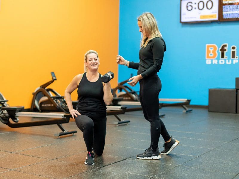 a certified personal trainer spots a gym member during a lunge exercise at a best fitness gym