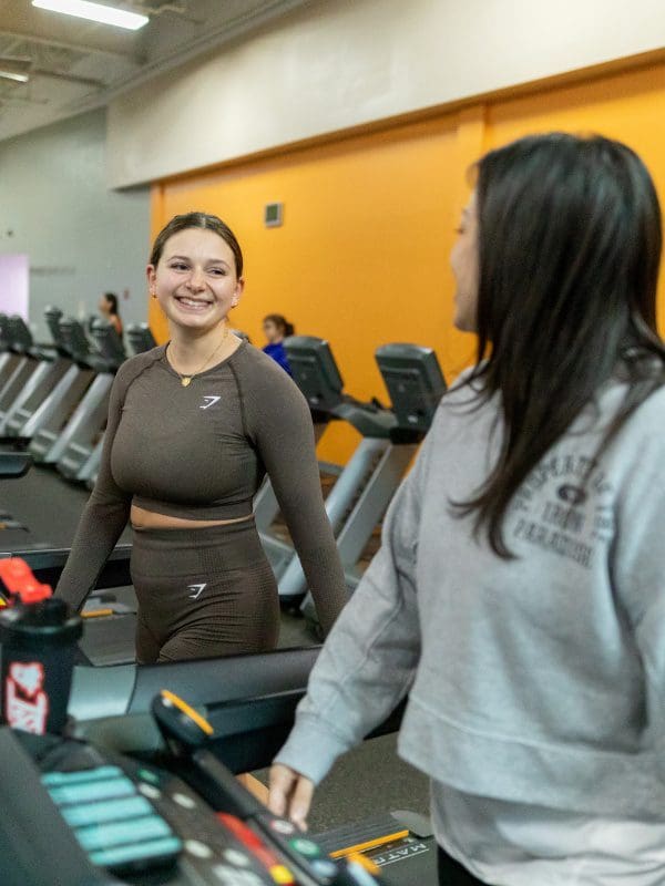 two gym members talk during a cardio workout on treadmills at a modern gym near me