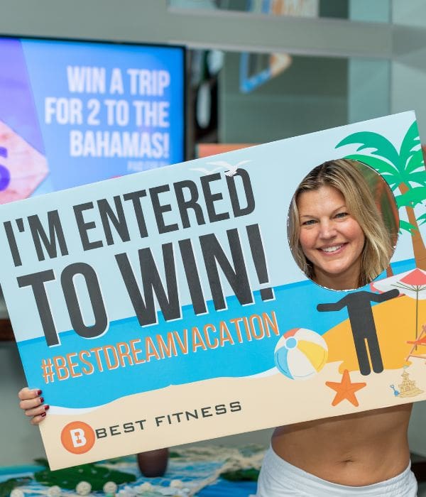 a best fitness team member holds a poster in front of her face promoting a dream vacation check in and win giveaway at best fitness gym