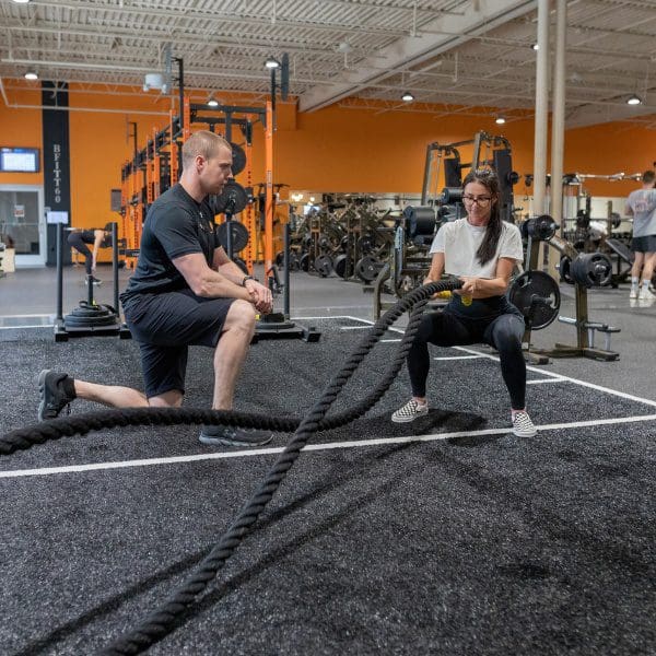 a certified personal trainer spots a gym member during a weighted ropes workout at a modern gym called best fitness